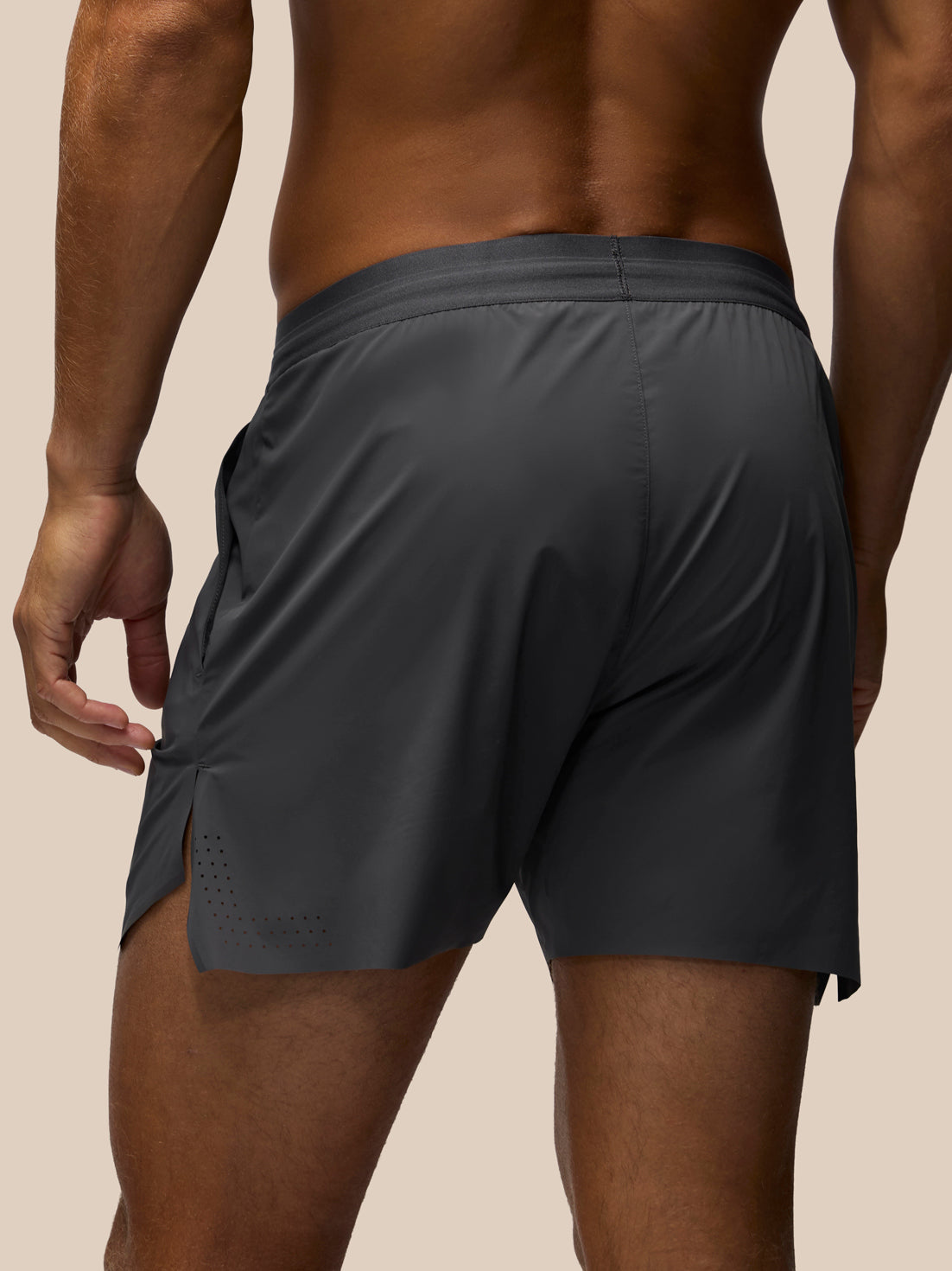 Rear view of a man wearing dark gray athletic shorts against a solid beige background.