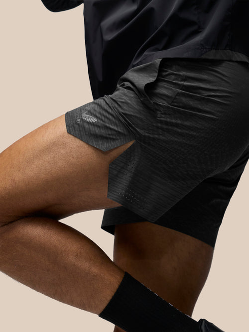 Close-up of a person wearing dark athletic shorts and a black top against a plain beige studio background.