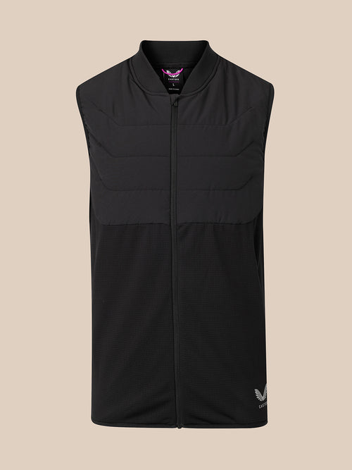 A black sleeveless zip-up vest with a mock neck and horizontal quilting, shown against a solid beige background. A small white logo is visible on the bottom right hem.