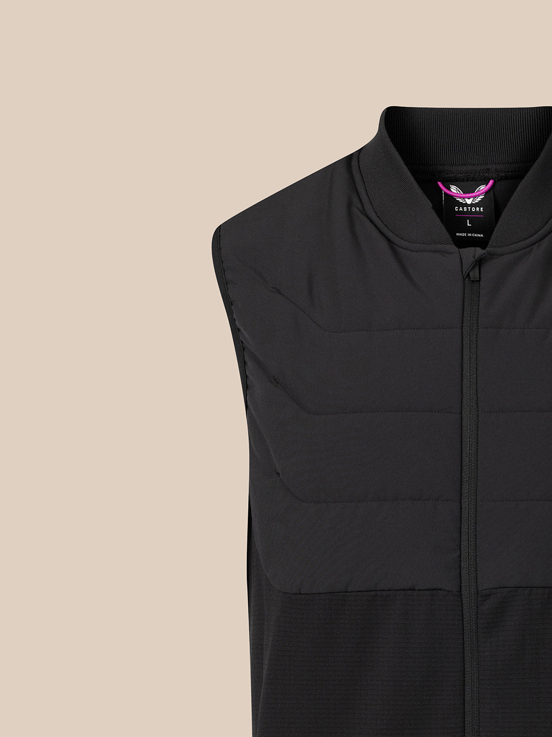 Close-up of a black sleeveless zip-front vest with horizontal quilting and a stand collar, shown against a plain warm beige background. A small purple and white neck label is visible.