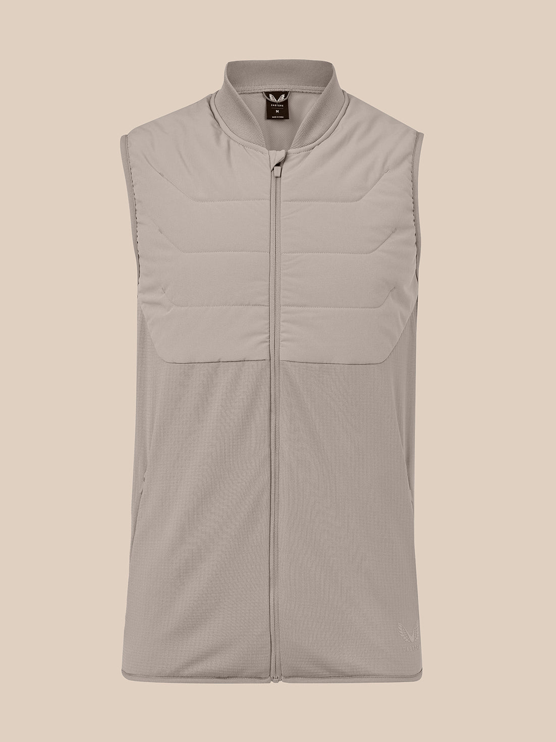 A sleeveless zip-front vest in a light taupe-beige color, featuring horizontal quilted paneling on the upper chest and a stand-up collar, shown against a solid beige background.