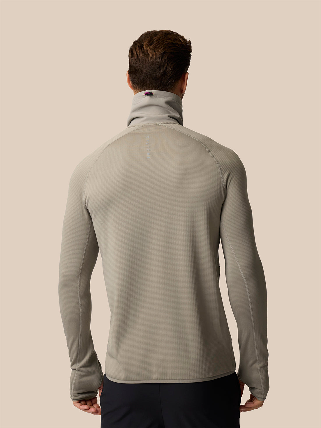 A man viewed from behind wearing a light gray long-sleeve athletic top with a high mock neck collar, set against a solid beige background.