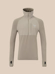 A long-sleeve quarter-zip pullover top in a light taupe-beige color, featuring a high mock neck collar, a vertical zippered chest pocket, and a small white wing logo on the left chest, displayed on a solid beige background.
