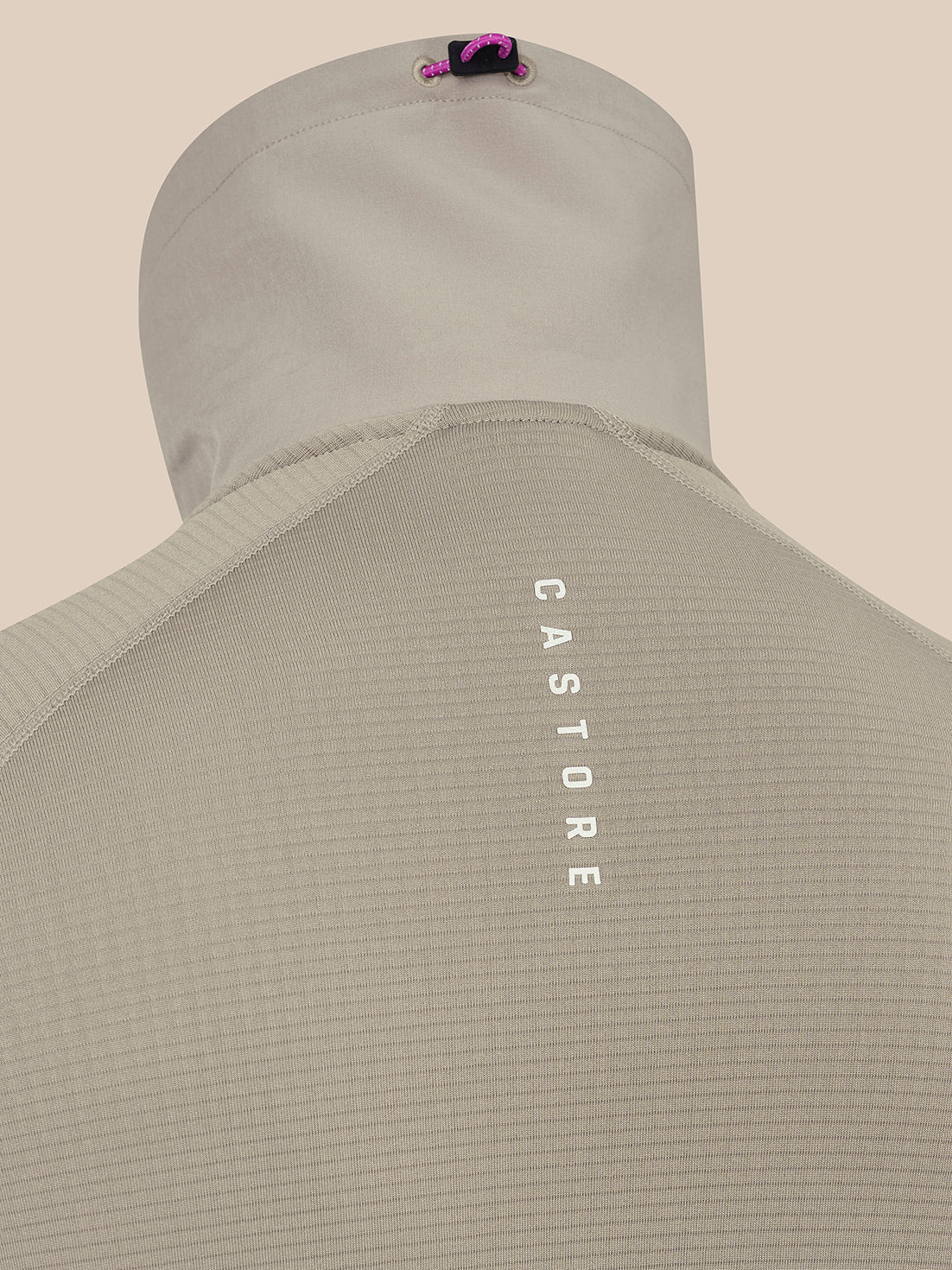 Close-up of the back of a light beige hooded top on a mannequin, showing vertical white 'CASTORE' text on the back and a small pink and black logo near the hood.