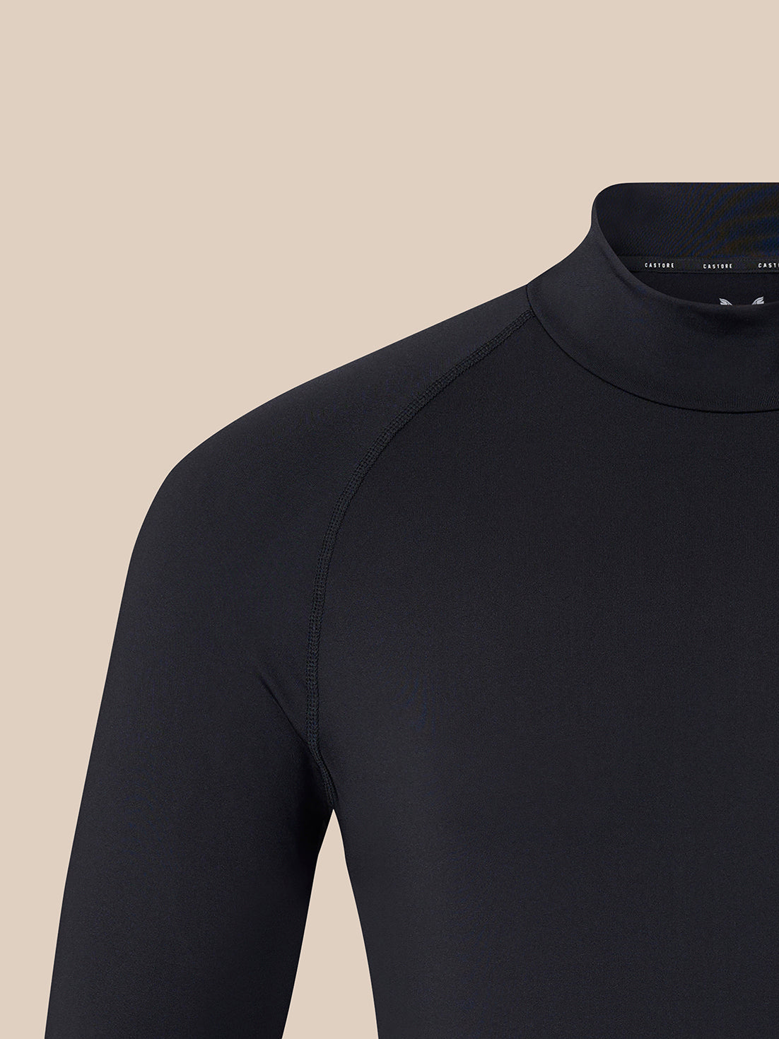 Close-up of a black long-sleeve mock neck top on a model, showing the shoulder and upper chest against a solid beige background.