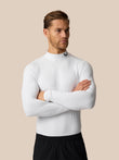 A man wearing a white long-sleeve mock neck athletic compression shirt, paired with black athletic shorts, standing against a solid beige background.