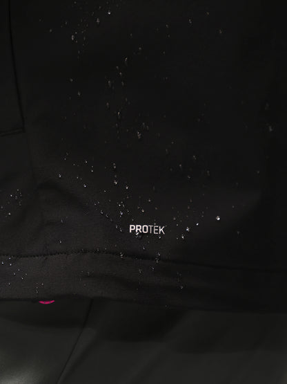 Close-up of a black waterproof jacket with water droplets beaded on the surface and the word 'PROTEK' printed in white near the bottom hem.