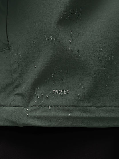 Close-up of a dark green waterproof fabric with water droplets beaded on the surface and the word PROTEK printed in white near the center.