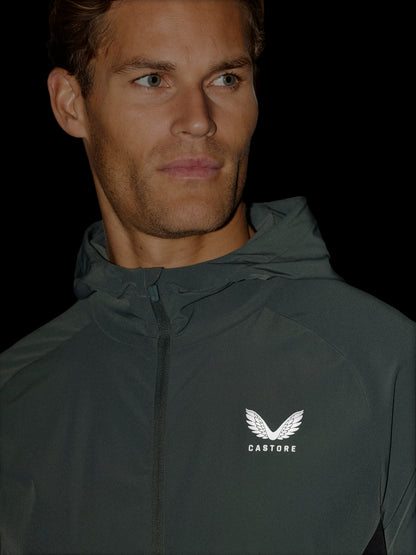 A close-up of a man wearing a dark gray hooded windbreaker jacket with a white wing logo and the brand name 'CASTORE' on the left chest, set against a solid black background.