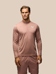 A man modeling a dusty rose long-sleeve athletic quarter-zip pullover with matching shorts against a solid beige background.