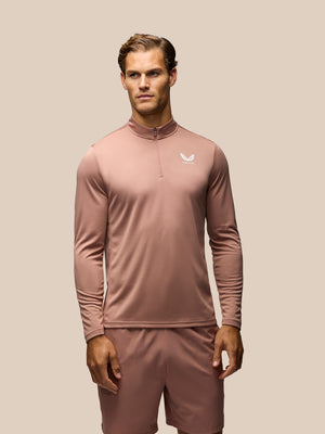 A man modeling a dusty rose long-sleeve athletic quarter-zip pullover with matching shorts against a solid beige background.