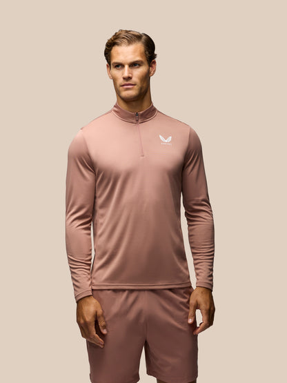 A man modeling a dusty rose long-sleeve athletic quarter-zip pullover with matching shorts against a solid beige background.