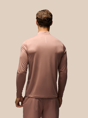 A man viewed from behind wearing a dusty rose long-sleeve athletic quarter-zip top and matching pants against a solid beige background.