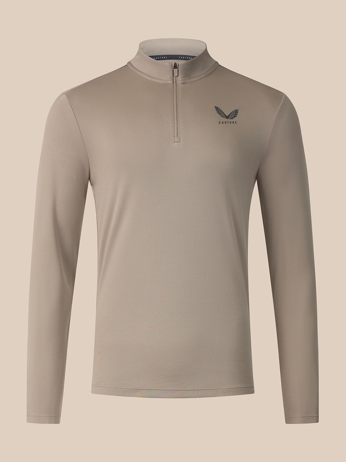 A long-sleeve quarter-zip athletic top in a light taupe-beige color, featuring a small dark gray wing logo and the brand name 'Castore on the left chest, displayed against a solid light beige background.