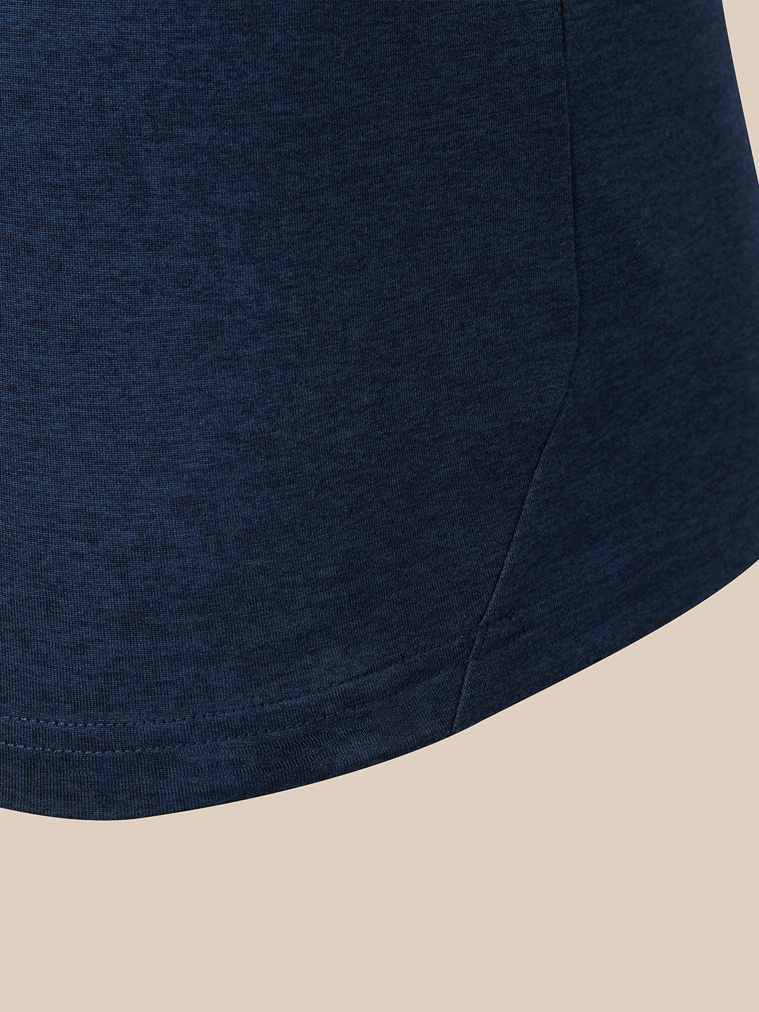Close-up of a dark navy blue heathered fabric garment corner with a curved hem, shown against a light beige background.