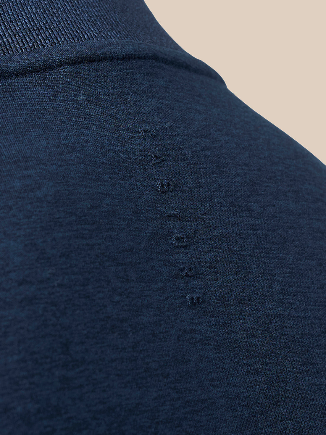 Close-up of a dark navy blue knit garment, showing the ribbed collar and a vertical row of small tonal embroidered letters on the chest.