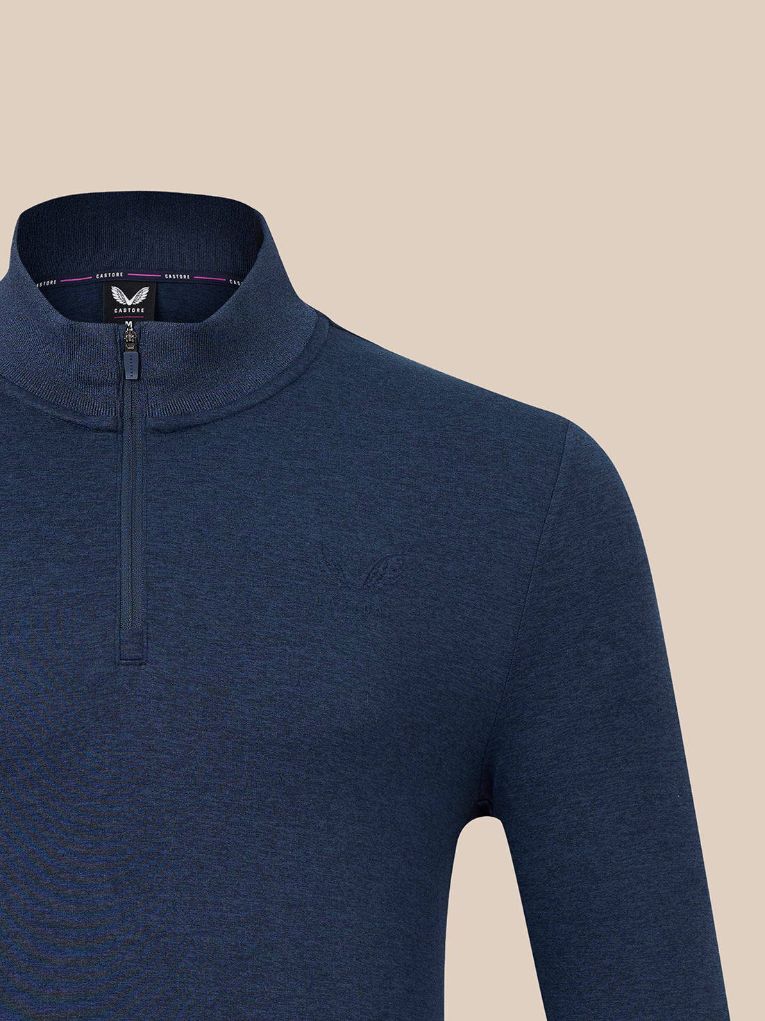 A close-up of a men's navy blue quarter-zip mock neck sweater from Castore, featuring a subtle tonal embroidered logo on the chest, set against a solid beige background.