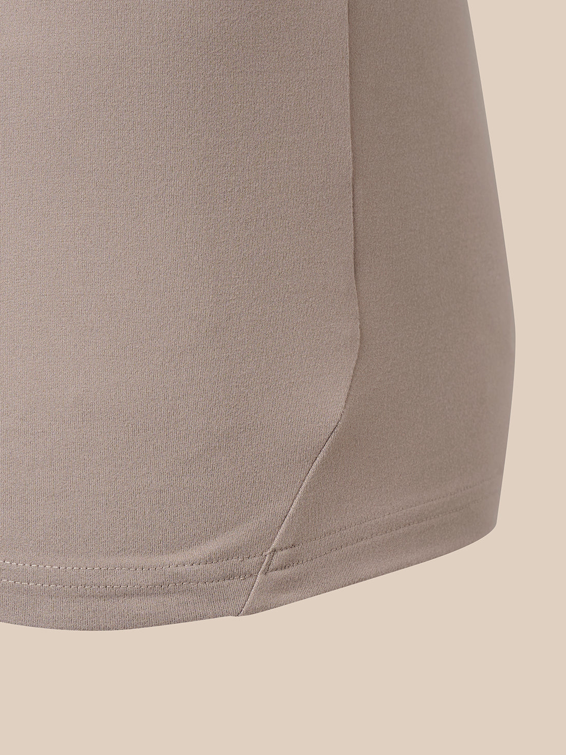 Close-up detail of a taupe-beige garment showing the side seam and hem stitching against a solid light beige background.