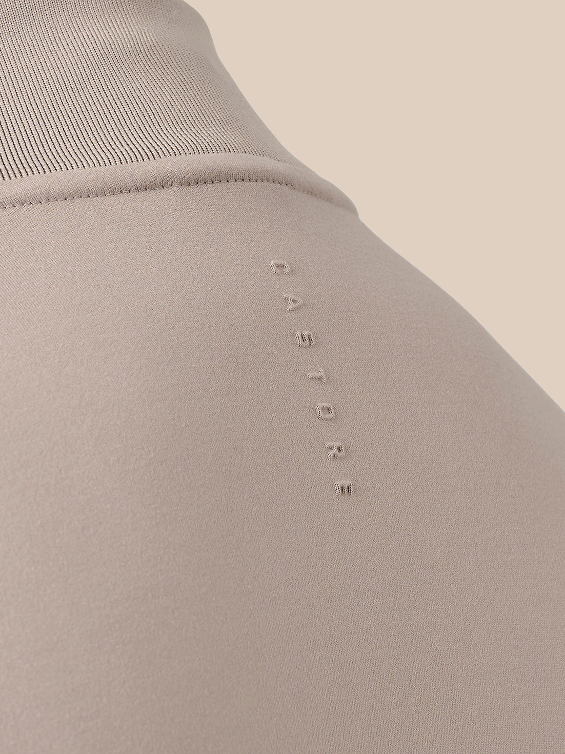 Close-up of a ribbed knit top in a light taupe-beige color, featuring the brand name 'CASTORE' vertically embroidered on the chest.