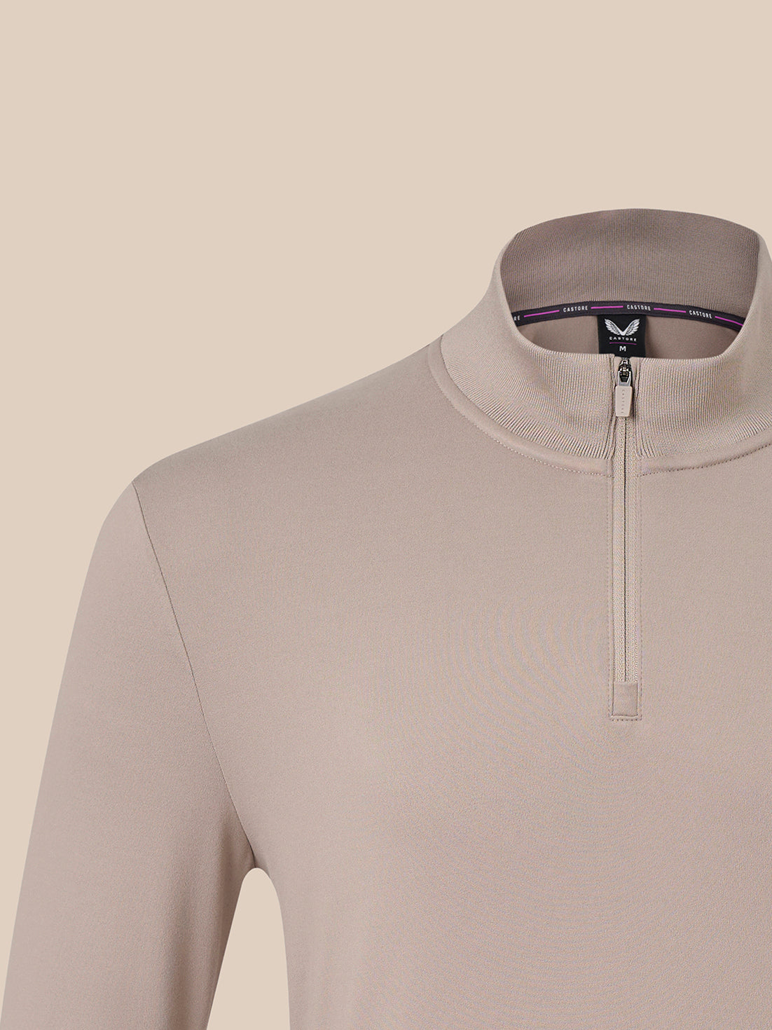 Close-up of a long-sleeve quarter-zip pullover in a light taupe-beige color, featuring a mock neck collar and a small black brand tag inside the collar.