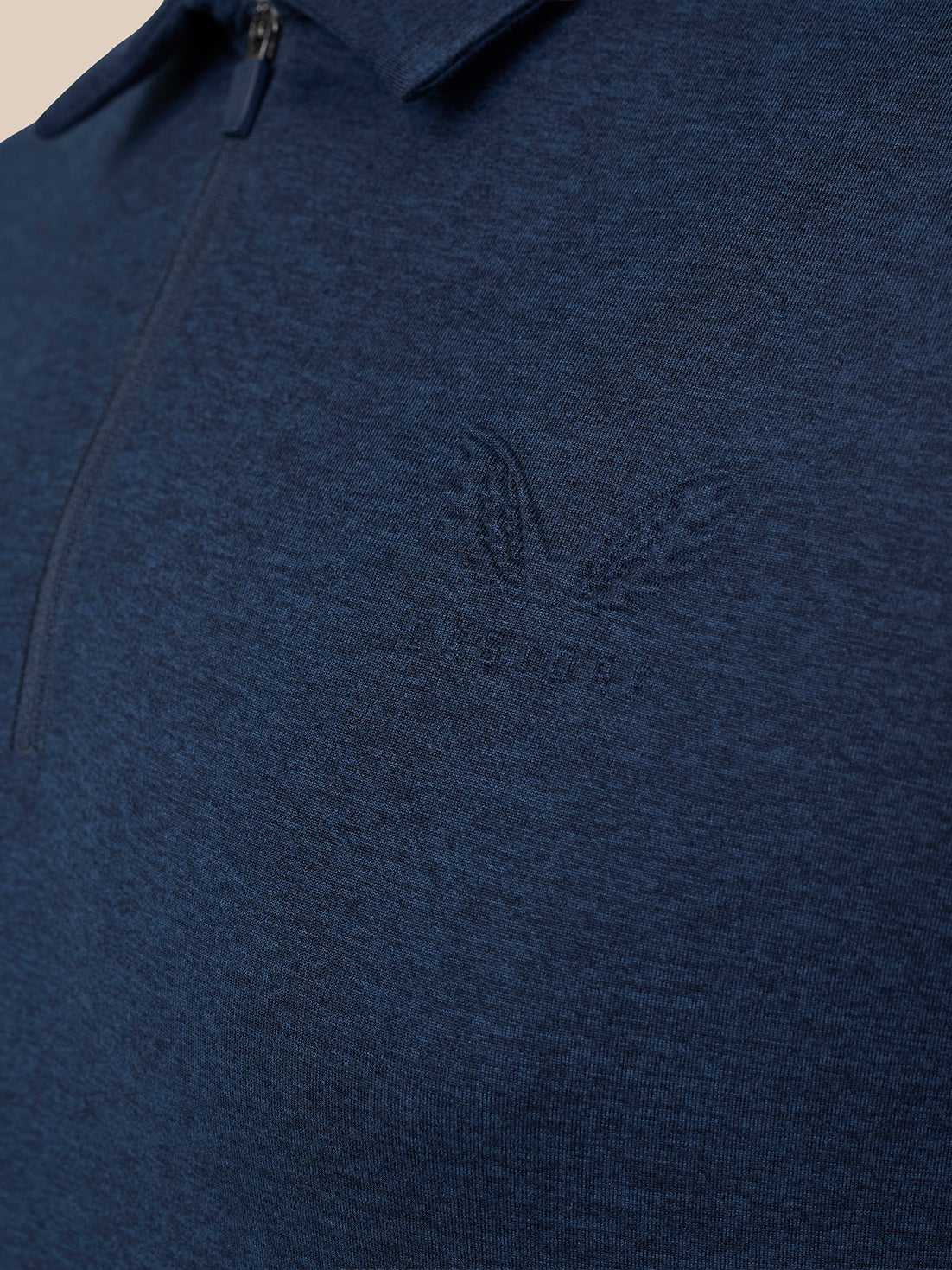 Close-up of a dark heather blue polo shirt with a subtle tonal embroidered logo on the chest.