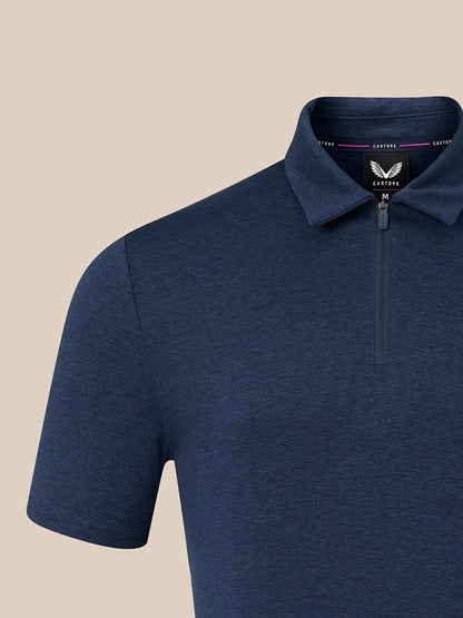 A close-up of a men's short-sleeve polo shirt in heathered navy blue, featuring a half-zip collar and a visible neck label for the brand 'Castorer'. The background is a solid, warm beige color.