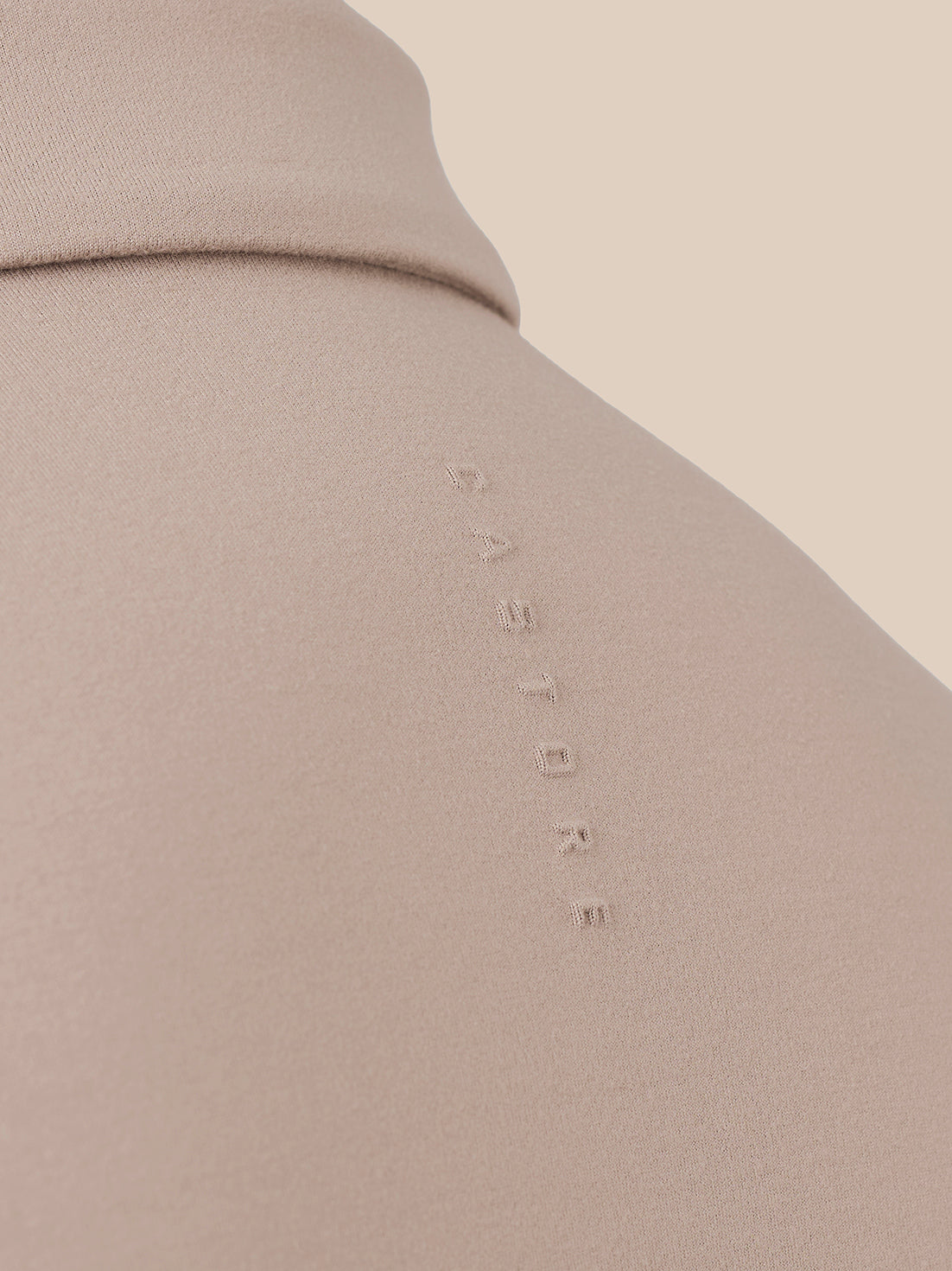 Close-up of a beige or taupe fabric surface with a small vertical debossed wordmark reading 'CASTORE' on the shoulder area.