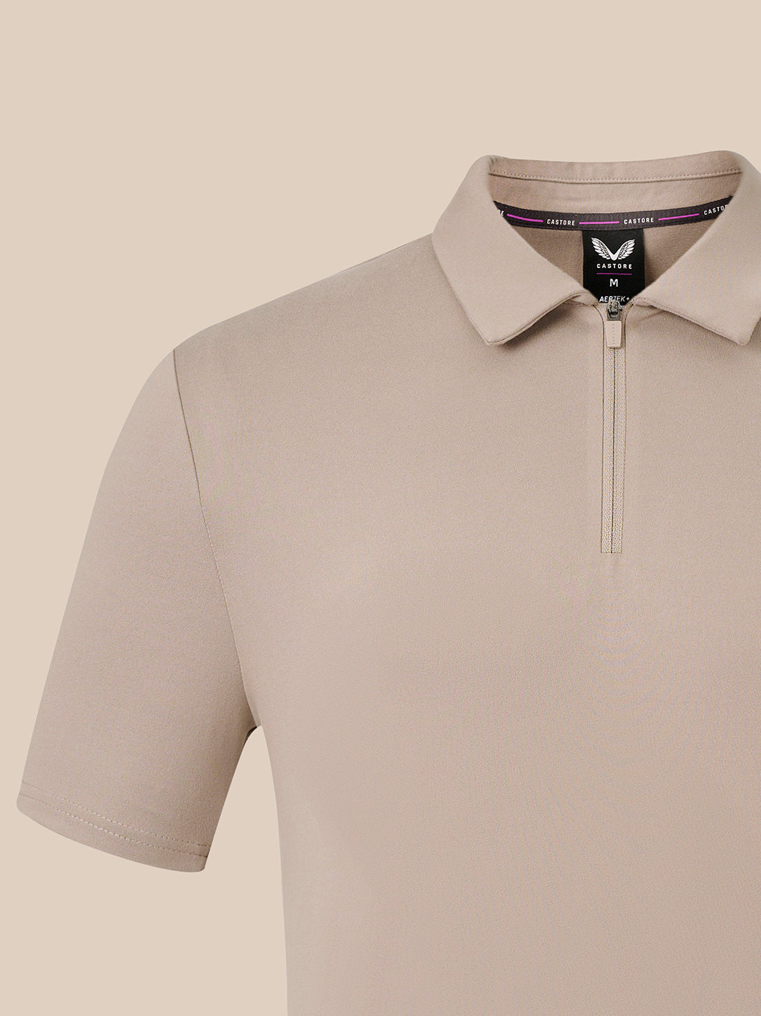 A close-up of a light beige short-sleeve polo shirt with a half-zip collar, shown on a solid beige background.