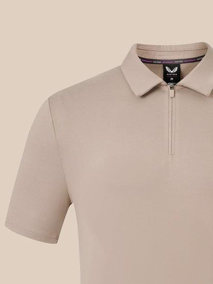 A close-up of a light beige short-sleeve polo shirt with a half-zip collar, shown on a solid beige background.