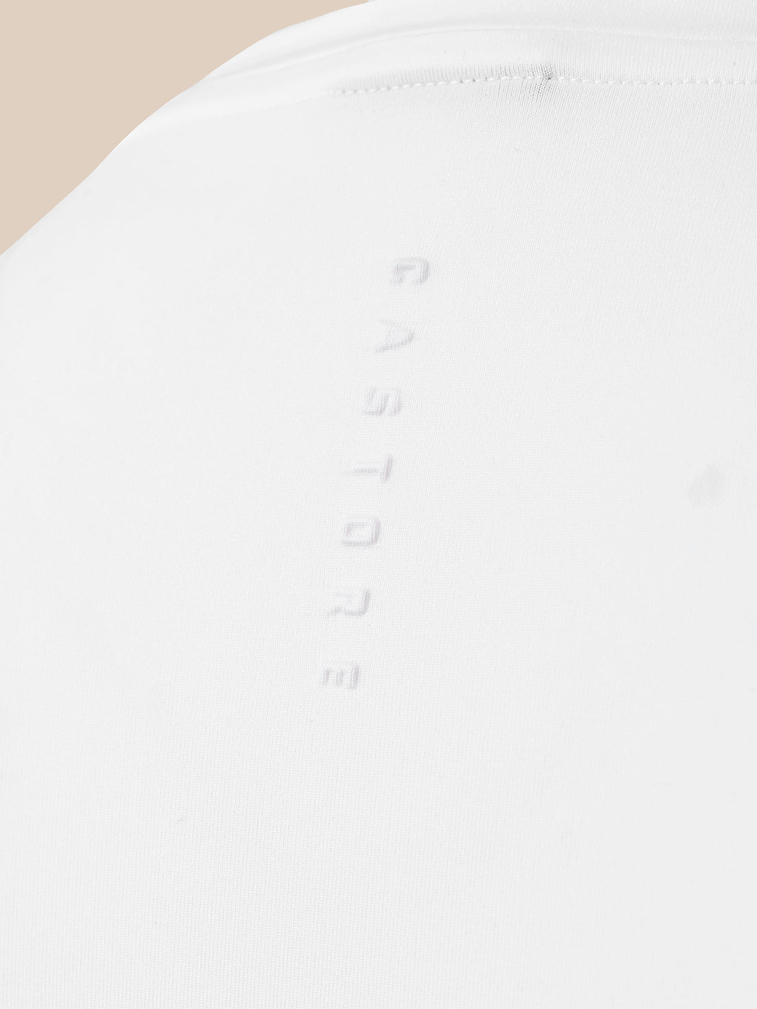 Close-up of a white fabric surface with a vertical embossed 'CASTORE' logo and a small stitched detail near the top, against a light beige background.