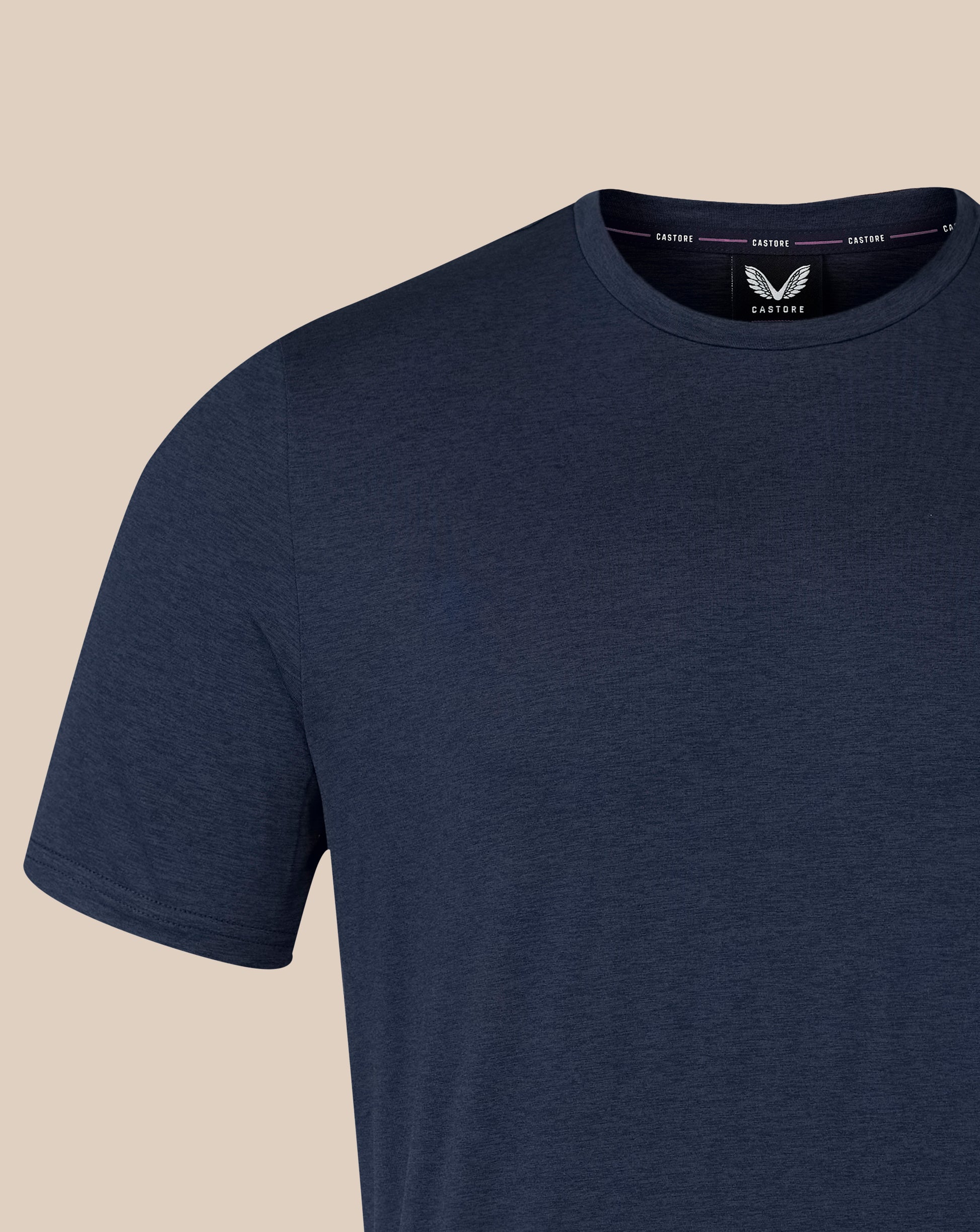 A close-up of a navy blue short-sleeve crewneck t-shirt by Castore, shown on a light beige background.