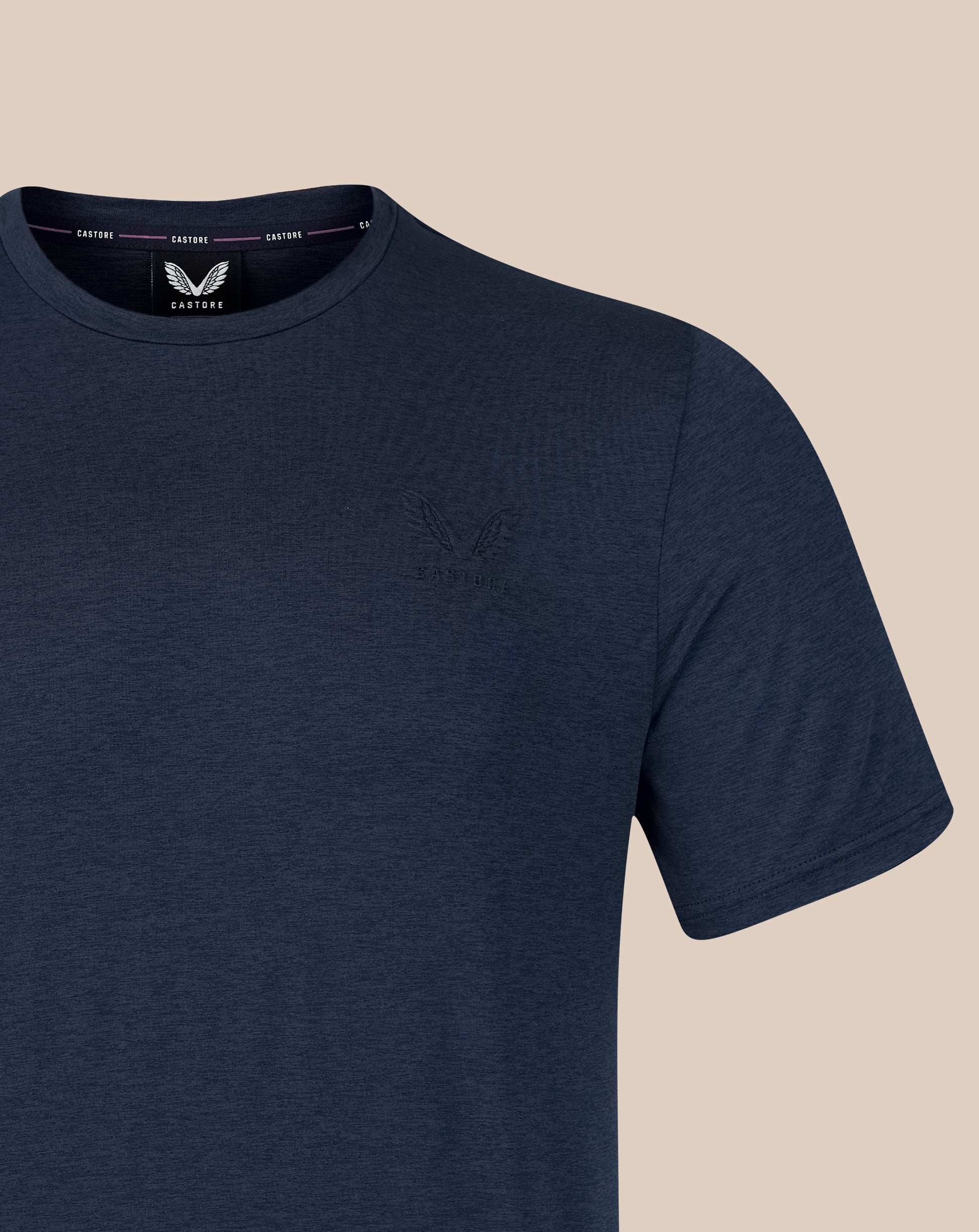 A close-up of a navy blue short-sleeve crewneck t-shirt by Castore, featuring a subtle tonal embroidered logo on the left chest and a visible brand label inside the collar.