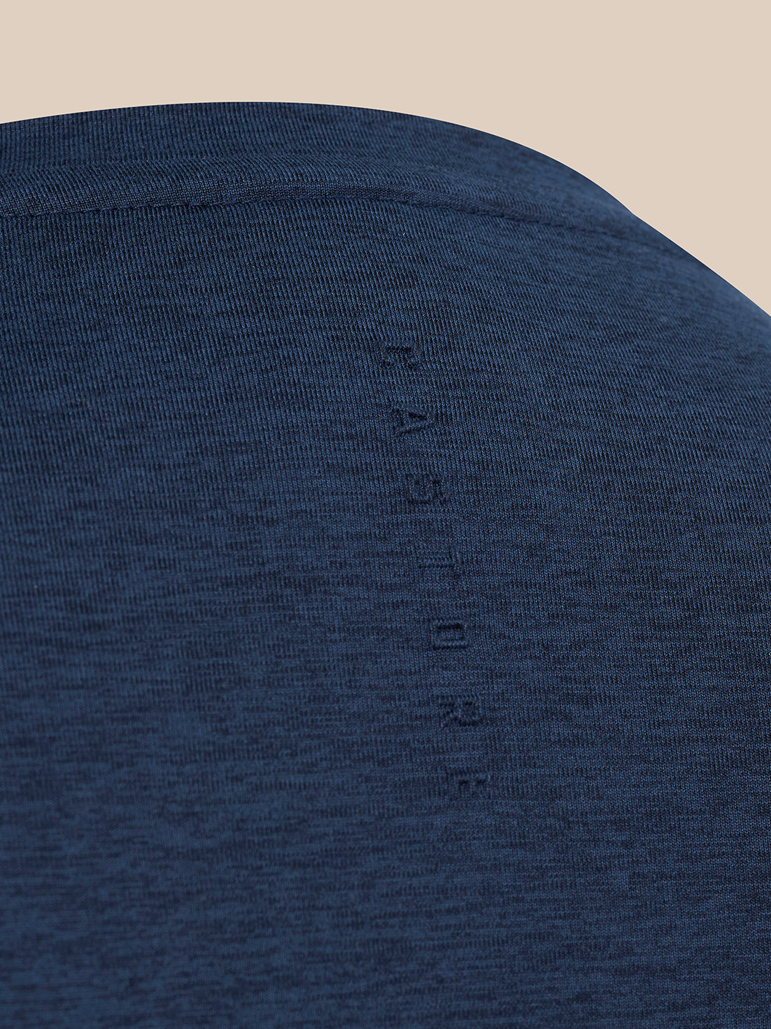Close-up of a dark heather blue knit fabric with a vertical tonal embroidered brand name reading 'Castore'.
