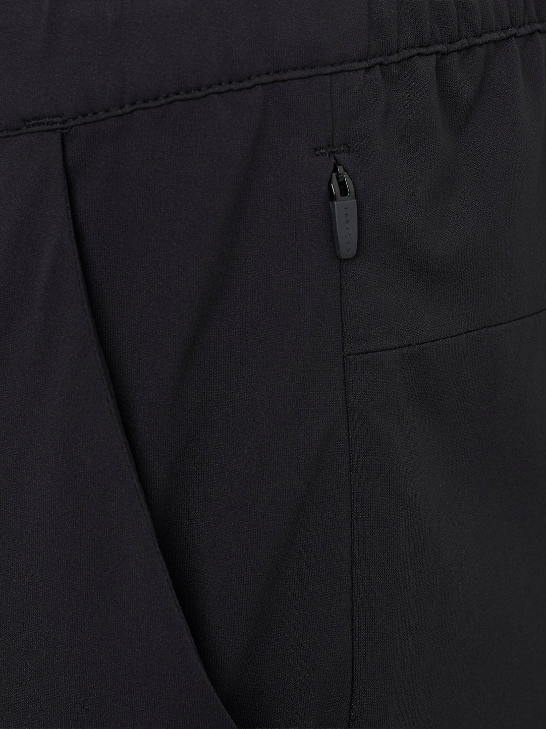 Close-up of a branded zipper pull on a back pocket of black trousers.