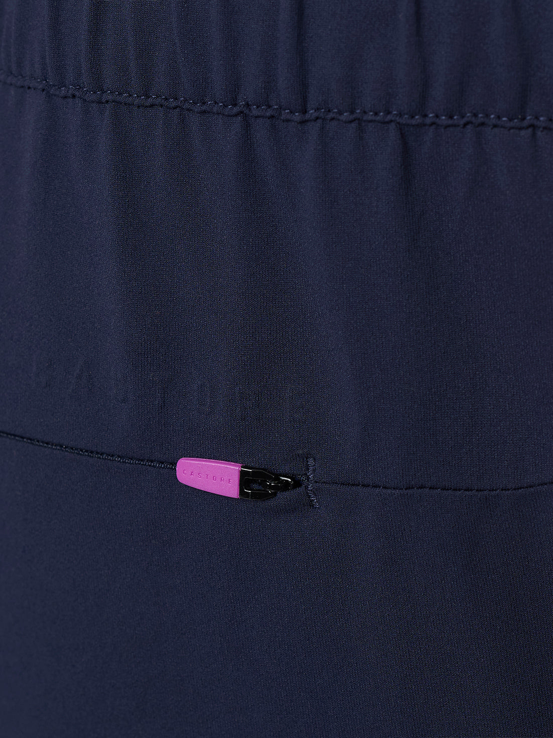 Close up detail of navy trousers featuring a back zip pocket and pink zipper pull
