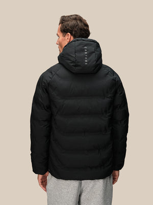 Back view of a man in a black padded hooded jacket with hood up and Castore branding on the hood