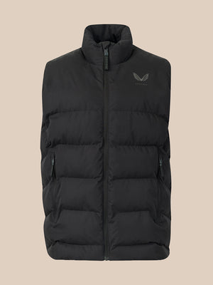 A black puffer vest with a stand-up collar and a small dark gray wing logo on the left chest, displayed against a solid beige background.