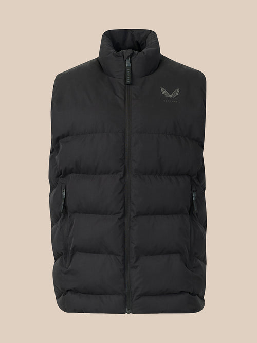 A black puffer vest with a stand-up collar and a small dark gray wing logo on the left chest, displayed against a solid beige background.