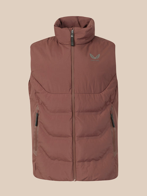 A sleeveless quilted puffer vest in a dusty rose-brown color, featuring a high collar, front zipper, and a small green wing logo on the left chest, set against a solid beige background.