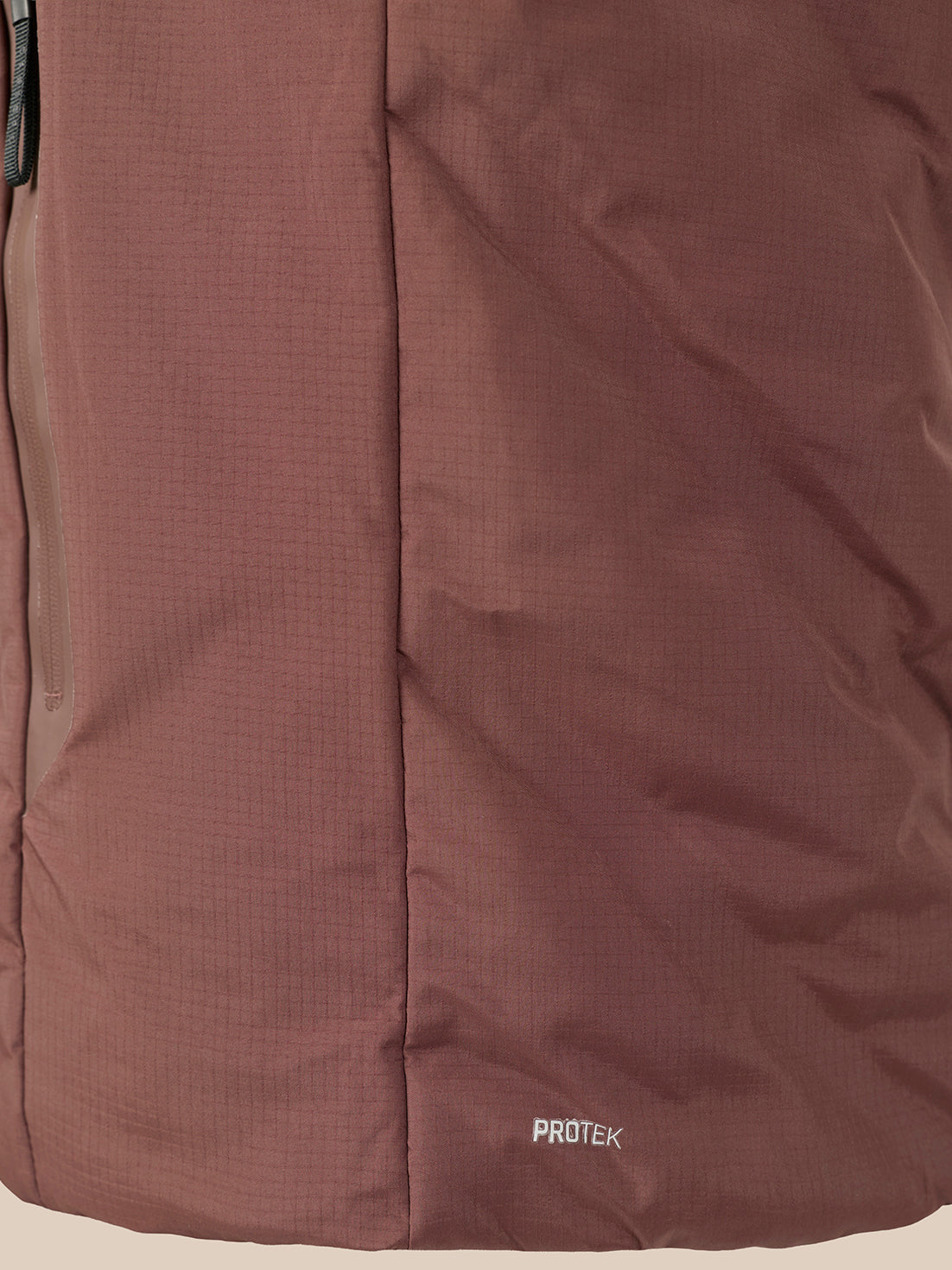 Close-up of a brown technical fabric jacket with a vertical seam and a small white 'PROTEK' logo near the bottom right.