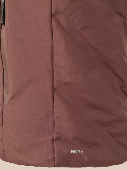 Close-up of a brown technical fabric jacket with a vertical seam and a small white 'PROTEK' logo near the bottom right.