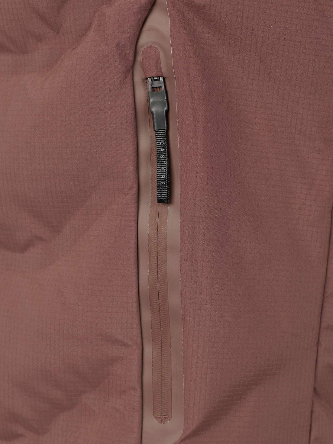 Close-up of a dusty rose puffer jacket with a vertical zippered pocket featuring a black textured zipper pull.