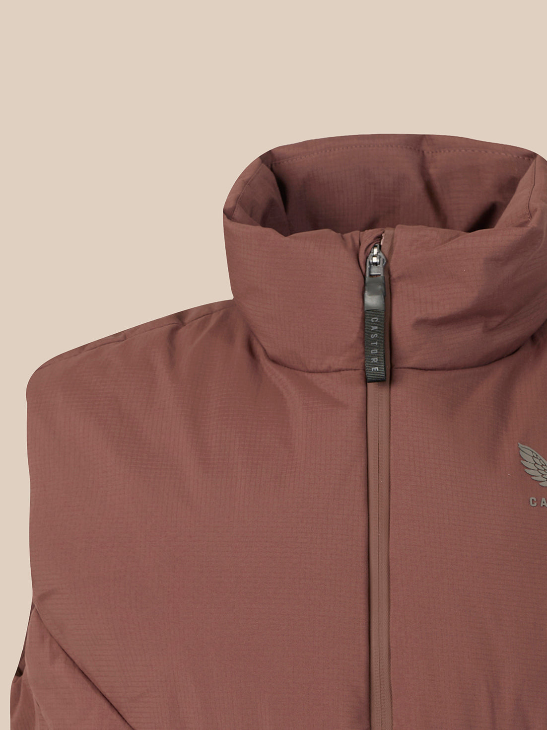 Close-up of a brown insulated jacket with a high stand-up collar, front zipper, and a small wing logo on the chest, shown against a plain beige background.
