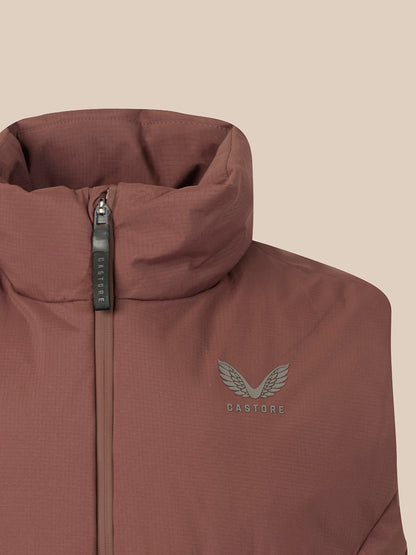 Close-up of a Castore jacket in a dusty rose-brown color, featuring a high collar, a dark gray zipper pull, and a matching gray embroidered wing logo on the chest.