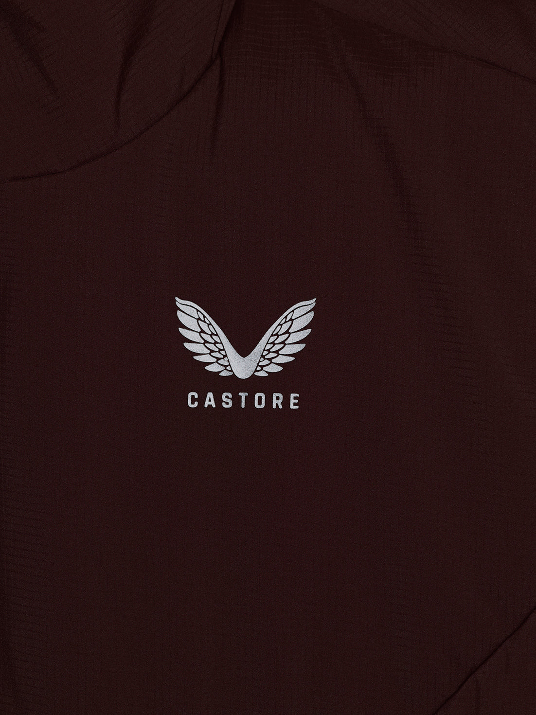 Close-up of a dark brown or very deep espresso-colored garment with a white embroidered wing logo and the word 'CASTORE' centered on the chest.