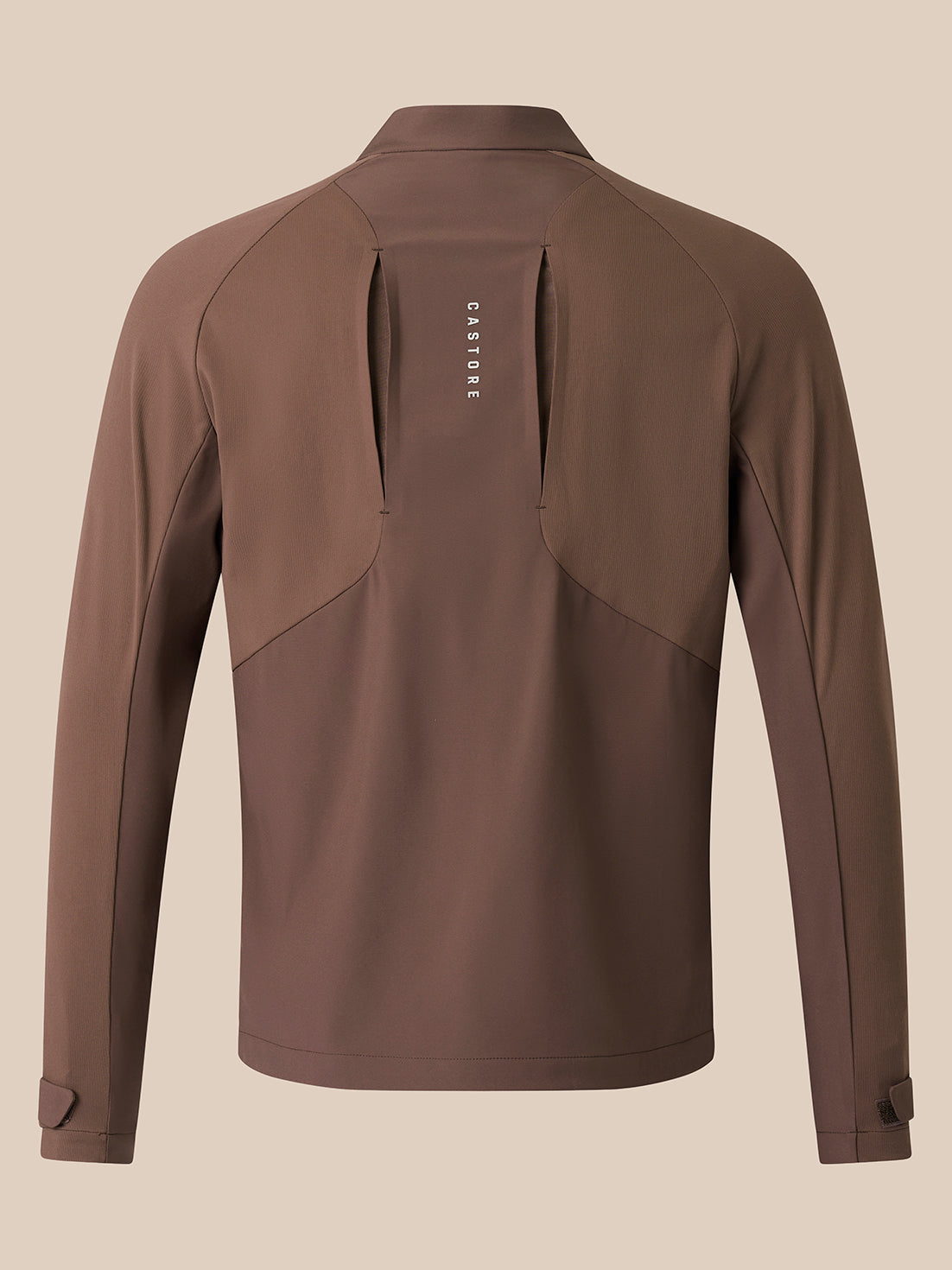 A brown long-sleeve athletic jacket shown from the back, featuring a vertical zippered pocket with the brand name 'Castore' printed in white, set against a solid beige background.