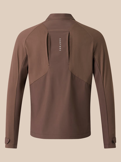 A brown long-sleeve athletic jacket shown from the back, featuring a vertical zippered pocket with the brand name 'Castore' printed in white, set against a solid beige background.
