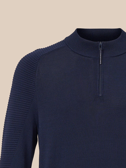 Close-up of a navy blue ribbed knit sweater with a quarter-zip mock neck and textured shoulder panels, shown against a solid beige background.
