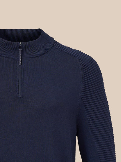 Close-up of a navy blue ribbed knit quarter-zip sweater with pleated shoulder detailing, shown against a solid beige background.