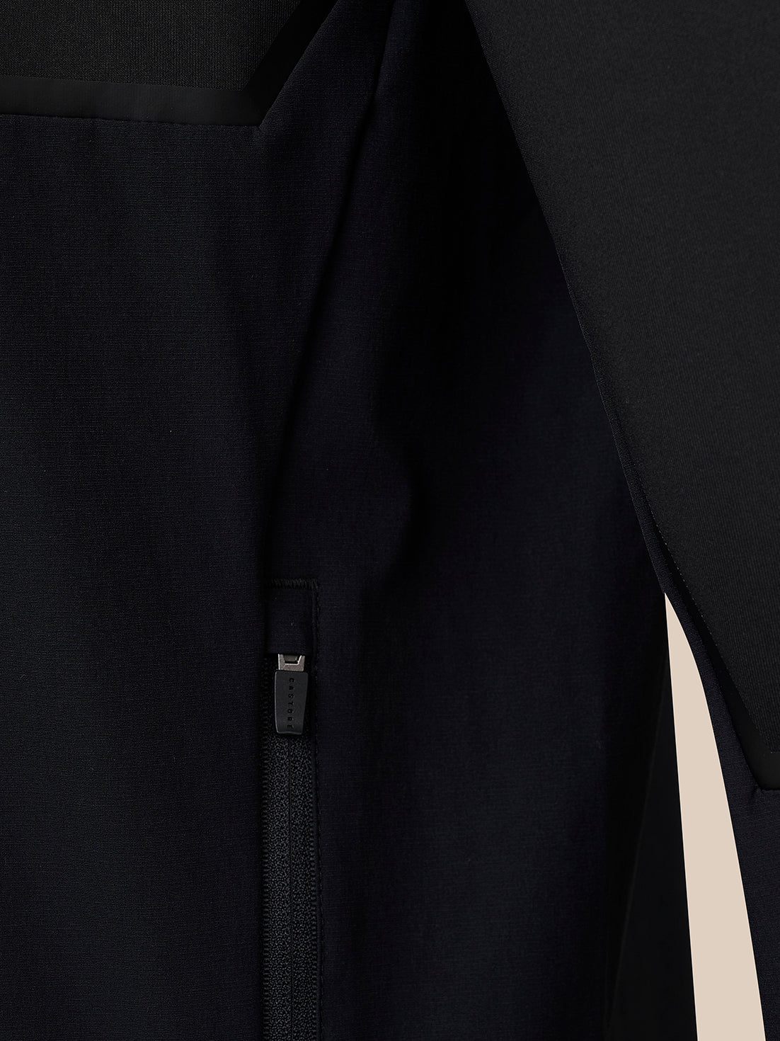Close-up detail of a black garment with a vertical zipper and a small fabric pull tab, shown against a dark background.